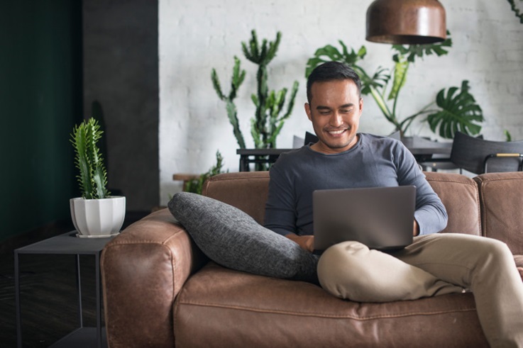 Asian man using laptop on a sofa at home