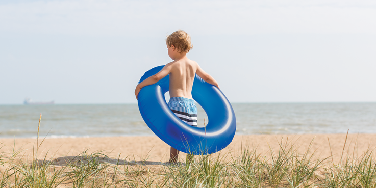 Little boy on beach holding inflatable ring around his waist
