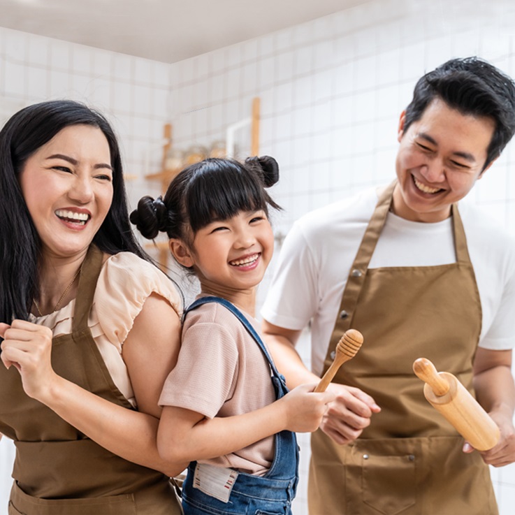 Asian father, mother and daughter in aprons working in kitchen happily.