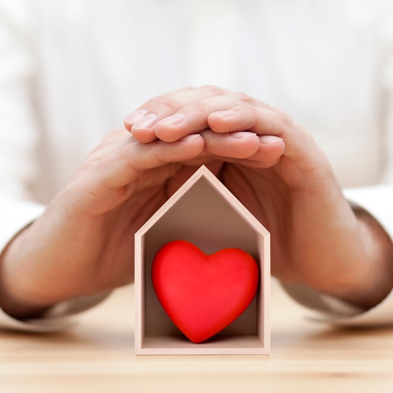 Hands cover a model house with a heart inside