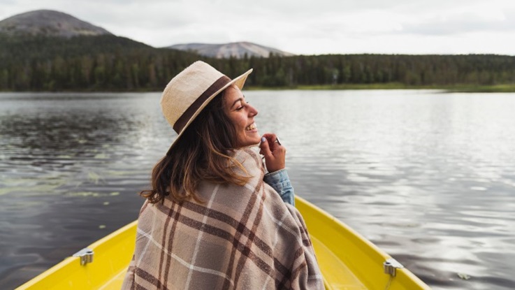 A happy woman wearing a hat on a boat on a lake in Finland